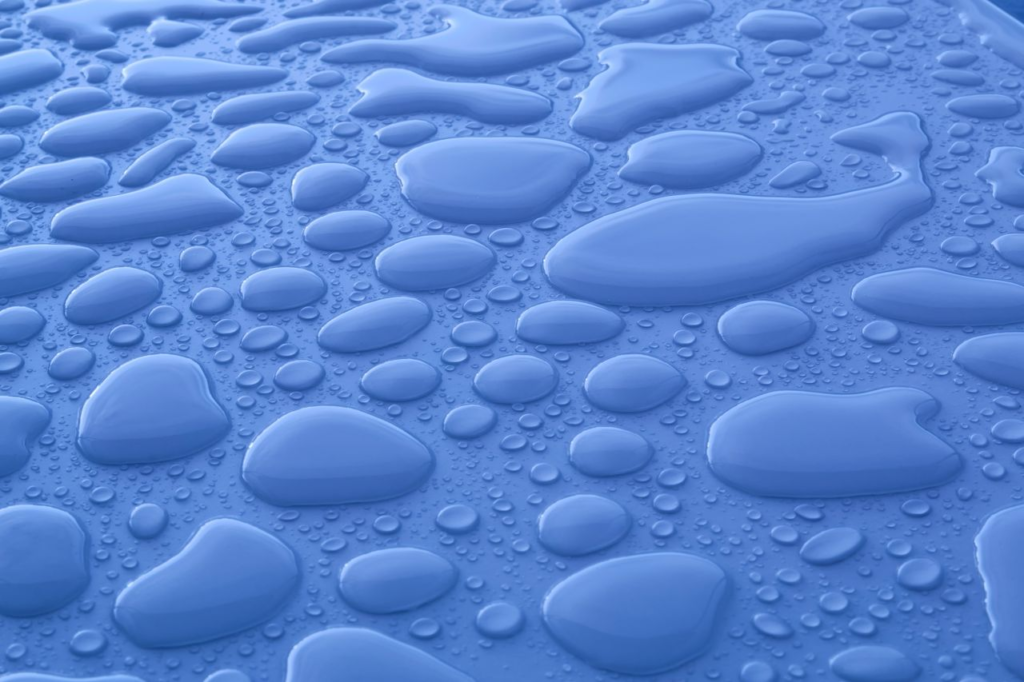 Closeup background of shiny blue surface with transparent liquid drops of different shapes